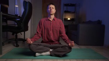 Evde nilüfer çiçeği pozuyla meditasyon yapan sakin bir genç adam. Farkındalık, rahatlama ve stres atımı.