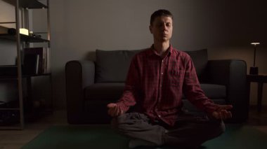 Evde nilüfer çiçeği pozuyla meditasyon yapan sakin bir genç adam. Farkındalık, rahatlama ve stres atımı.