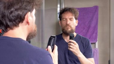 Adam uzun sakalını jilet makinesiyle yavaş çekimde tıraş ediyor.