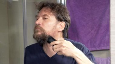 Adam tıraş makinesiyle uzun sakal kesmeye başlıyor.
