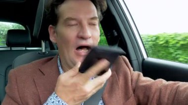  Havalı iş adamı araba kullanırken telefonla sesli mesaj kaydediyor..