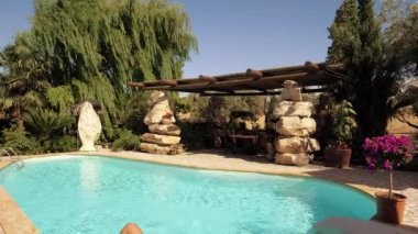  Gün batımında yüzme havuzunda güneşlenen mutlu genç kadın. Ağır çekim.