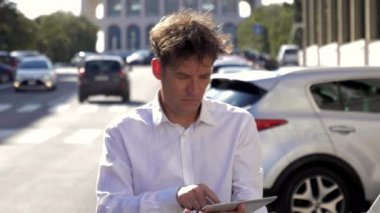 Şehir yavaş gün batımında tablet ile sokakta çalışan serin iş adamı