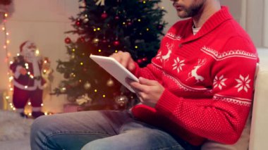 adam kanepede oturan ve dekore edilmiş Noel oturma odasında tablet kullanarak kırpılmış atış