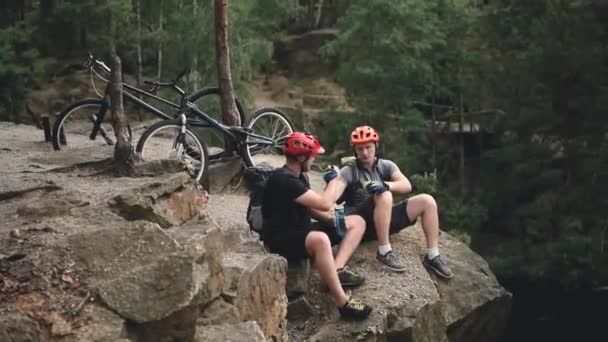 Пробні Велосипедисти Шоломах Тримаючи Руки Відпочиваючи Скелі Велосипедами Позаду Сосновому — стокове відео