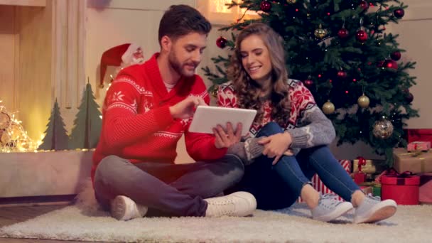 快乐的年轻夫妇坐在地板上使用平板电脑一起在圣诞节 — 图库视频影像