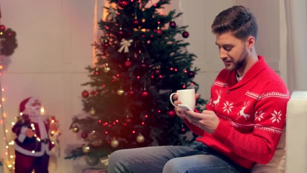 Joven Feliz Sentado Sofá Con Una Taza Café Uso Teléfono — Vídeo de stock