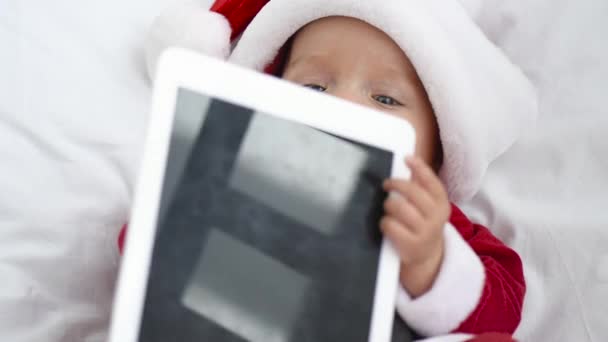 サンタ衣装クリスマス コンセプト 自宅のまぐさ桶で空白の画面とタブレットで遊ぶかわいい赤ちゃん — ストック動画