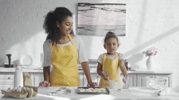 愛らしいアフリカ系アメリカ人子供エプロン キッチンの近くに立っている彼女の母ながら小麦粉を楽しんで — ストック動画