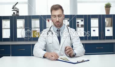 tanısı ile masada oturan, sayma ve cebinde para koyarak beyaz montlu erkek doktor