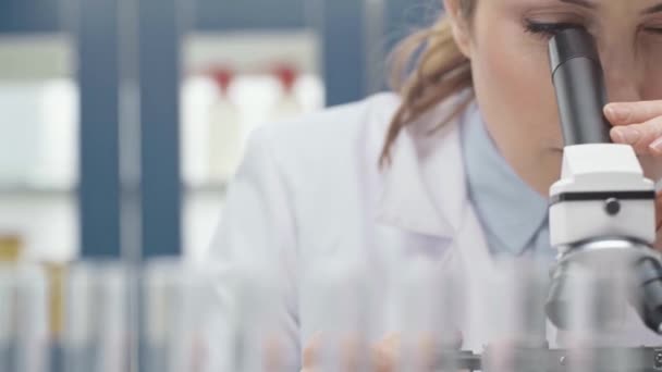 研究室で顕微鏡を通して見る白衣の女性科学者 — ストック動画
