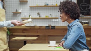 Afrikalı-Amerikalı kadın müşteri kafede börekler, çörekler ve macarons için güzel getiren kadın garson gülümseyerek