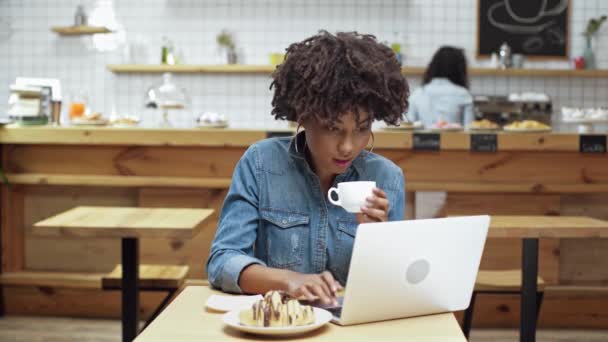 美丽的非洲裔美国女性自由职业者坐在桌子上 喝咖啡 并在咖啡馆使用笔记本电脑 — 图库视频影像