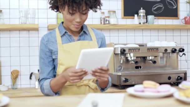 krásný usměvavý africké americké ženské pokladník pomocí digitálních tablet za pultem se zákusky v kavárně 