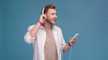 mutlu yakışıklı smartphone cep telefonu ile müzik ve dans mavi izole kulaklık