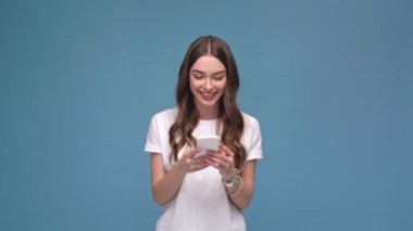 Smartphone kullanarak ve üzerinde izole mavi kopya alanı ile gülümseyen güzel kız