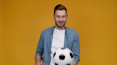 yakışıklı adam iplik futbol topu parmağına, gülümseyen, kameraya bakıyor ve sarı izole işareti yukarı gösteren
