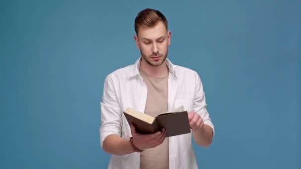 Guapo Hombre Insatisfecho Leyendo Libro Aislado Azul — Vídeos de Stock