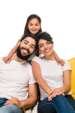 happy latin parents smiling while sitting on sofa near daughter isolated on white  clipart