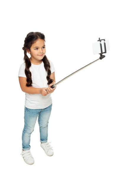 overhead view of happy latin kid holding selfie stick while taking selfie isolated on white 