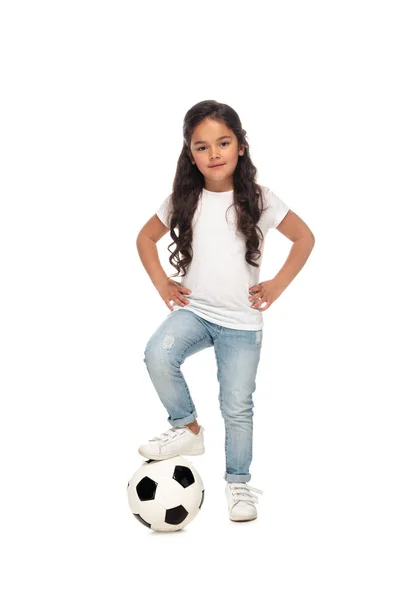 白で隔離されたサッカーの近くに腰に手を置く陽気なラテンの子供 — ストック写真
