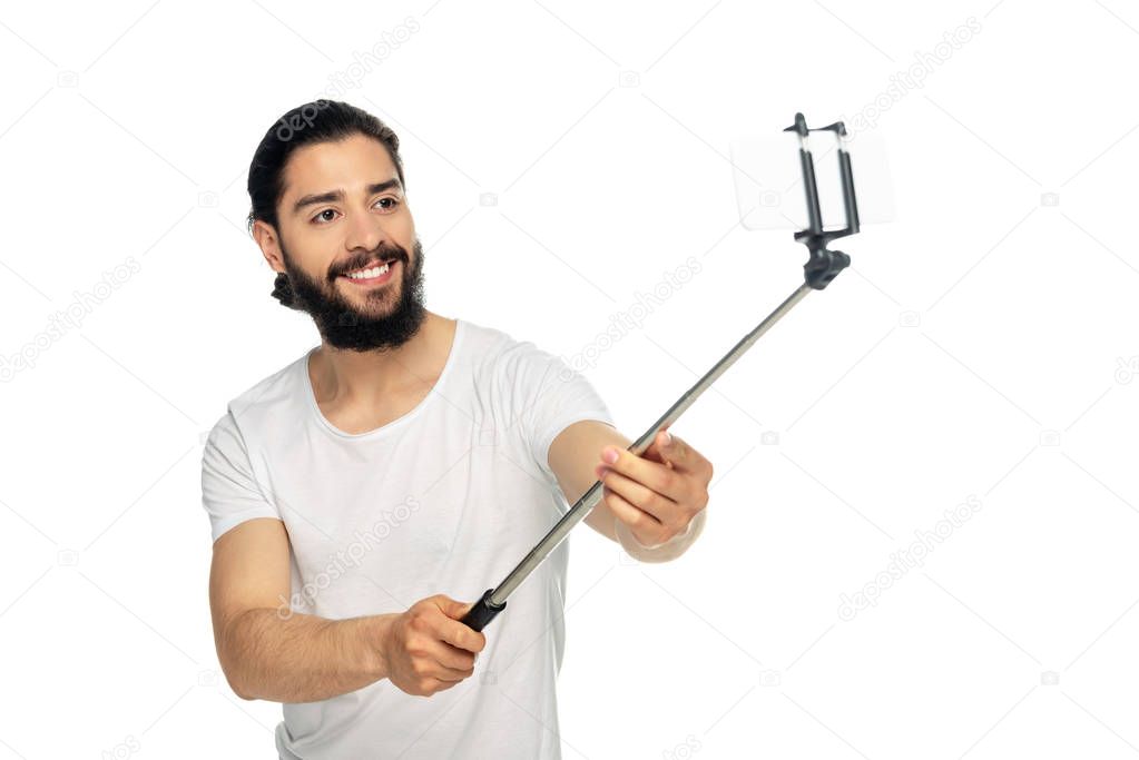 happy latin man holding selfie stick while taking selfie isolated on white 