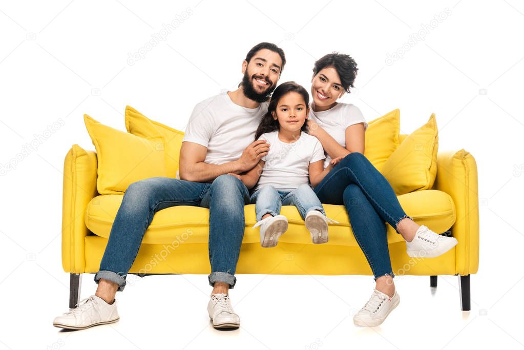 happy latin parents smiling while sitting on sofa with adorable daughter isolated on white 
