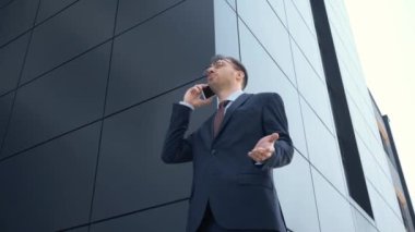 akıllı telefon kullanan işadamının düşük açı görünümü, bina yakınında gesturing ve gülümseyerek