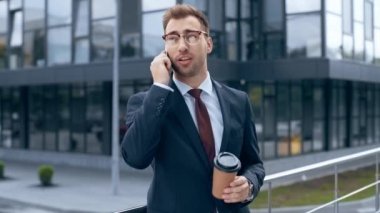 akıllı telefon dan konuşan işadamı, gülümseyerek, gülerek ve bina yakın gitmek için kahve içme 