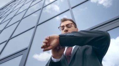 saat bakarak ve binanın yakınında etrafa bakan işadamı nın düşük açı görünümü