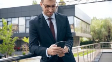 akıllı telefon kullanan işadamı, gülümseyen ve bina yakın gitmek için kahve içme