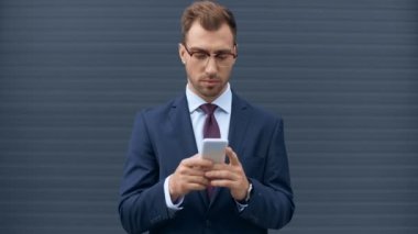 akıllı telefon kullanan işadamı, gülümseyen ve gri duvara yakın sıkıştırılmış yumruk ile tezahürat