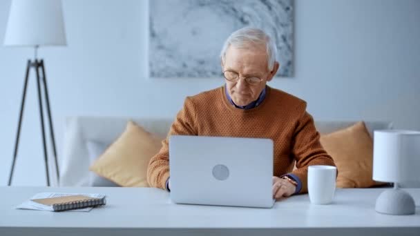 Senior Man Tar Glasögon Skriva Laptop Och Dricka Hemma — Stockvideo