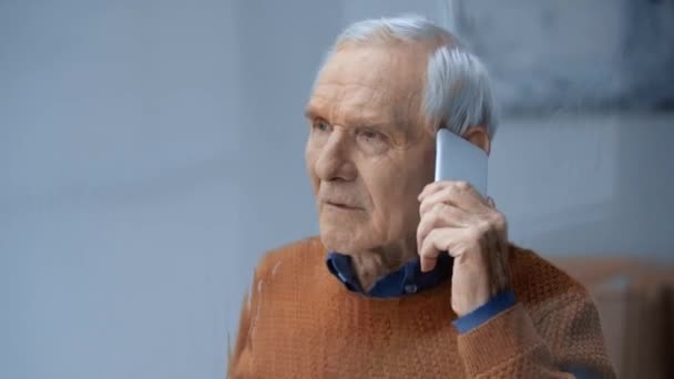 雨が降る窓の近くでスマートフォンで話す先輩男性の選択的な焦点 — ストック動画