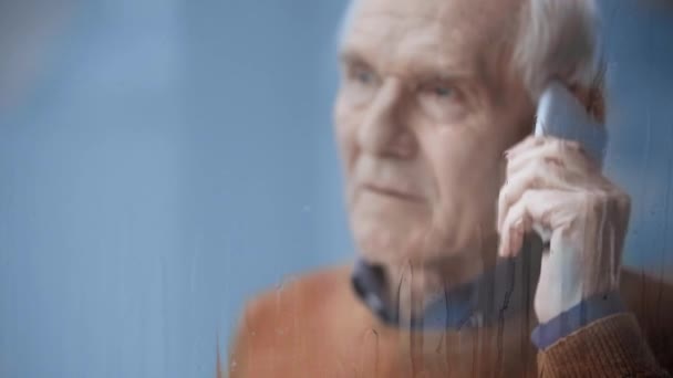 スマートフォンで話す先輩男性の近くに雨を注ぐ窓の選択的な焦点 — ストック動画