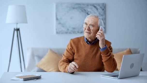 Happy Senior Man Tar Smartphone Och Pratar Nära Laptop Hemma — Stockvideo