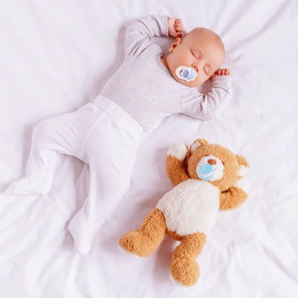 High angle view of adorable little boy with baby dummy sleeping with teddy bear — Stock Photo