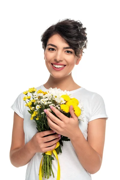 Mujer latina feliz mirando a la cámara mientras sostiene flores amarillas aisladas en blanco - foto de stock