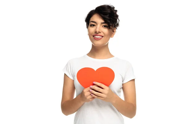 Cheerful latin woman holding red heart-shape carton isolated on white — Stock Photo
