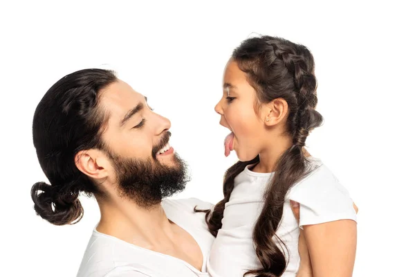 Щасливий латинський батько посміхається, дивлячись на милу дочку, що показує язик ізольовано на білому — стокове фото