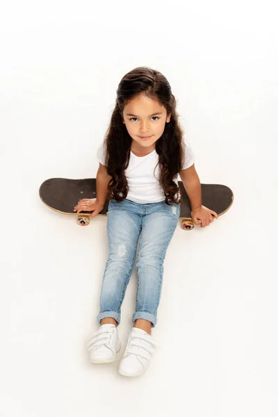 Overhead view of cute latin kid sitting on penny board isolated on white — Stock Photo