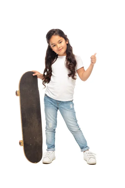 Carino bambino latino mostrando pollice in su, mentre tenendo penny board isolato su bianco — Foto stock