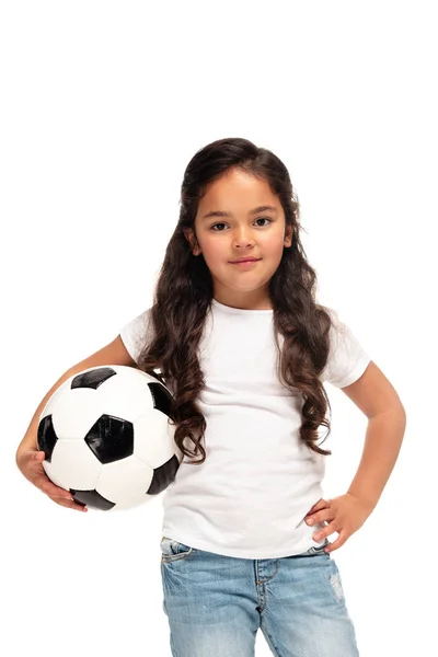 Cheerful latin kid standing with hand in hip and holding soccer ball isolated on white — Stock Photo