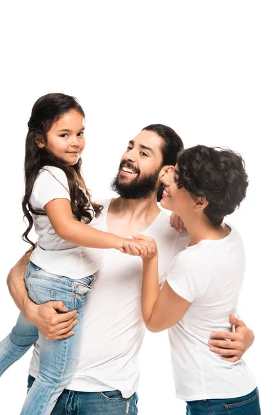 Feliz latino sosteniendo en brazos adorable hija mientras sonríe cerca de esposa aislado en blanco - foto de stock