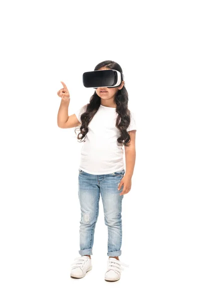 Niño latino señalando con el dedo mientras usa auriculares de realidad virtual aislados en blanco - foto de stock