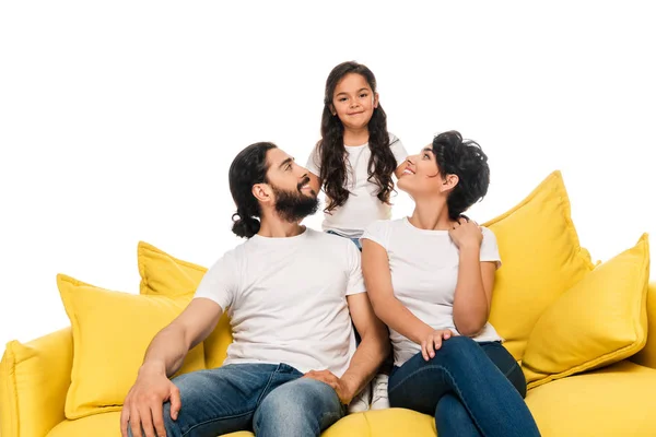 Smiling latin parents sitting on sofa and looking at cute daughter isolated on white — Stock Photo