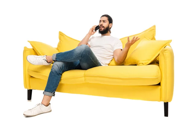 Mécontent latin homme parler sur smartphone tandis que assis sur canapé jaune isolé sur blanc — Photo de stock