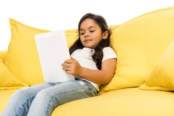 Vista a basso angolo del bambino latino utilizzando tablet digitale mentre seduto sul divano isolato su bianco — Foto stock
