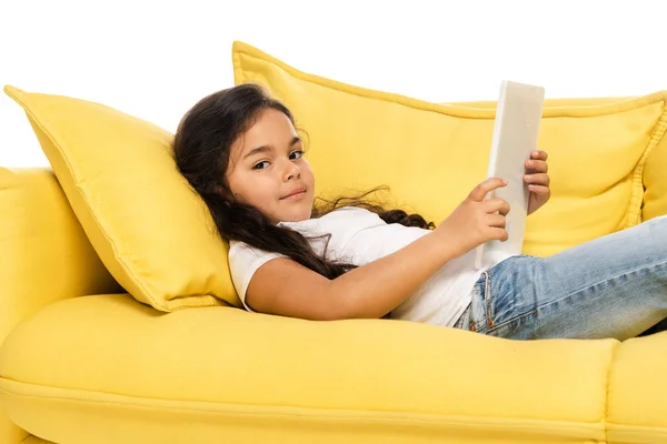 Happy latin kid using digital tablet while lying on sofa isolated on white — Stock Photo