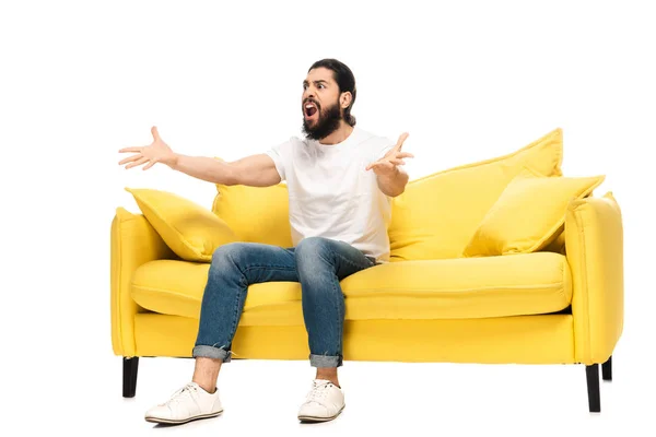 Barbuto uomo latino guardando campionato mentre seduto sul divano e gesticolando isolato su bianco — Foto stock